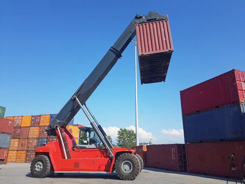 Reach stacker lifting a shipping container at a busy cargo terminal, illustrating global logistics, container handling, freight transportation, port operations, and supply chain efficiency.