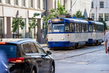 Fototapeta premium Traditional two car electric streetcar moving through a historic urban district on a sunny day highlighting municipal passenger transportation