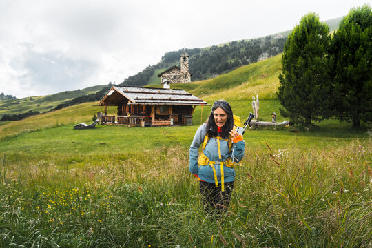 Disgusted woman hiker in waterproof clothing pulling funny face walking facing fears in tall high wet wildflower meadow background Malga Rossalm loop trail outdoor wilderness.Dolomites Italy