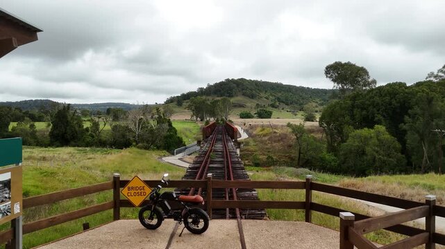 E-bike parked at a rest stop and old train bridge along the Lismore section of the The Northern Rivers Rail Trail. Moving drone view