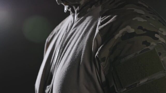 Studio light causing man breathing and tilting collar showcasing camo sleeve velcro patch on hoodie