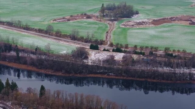 Drone panorama reveals patchy snow farmland bordering reflective waterway