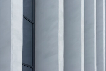 Naklejka premium Minimalist building facade with vertical white columns and a dark window strip. Gray architectural wall with clean lines and repeating surfaces.