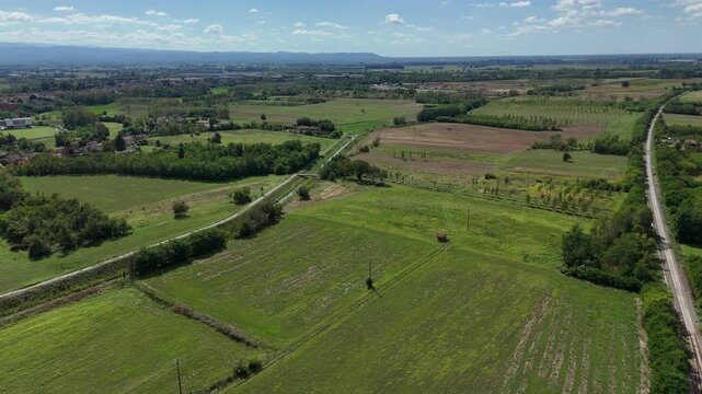 Agricultural fields, drainage corridors and rural roads form a geometric landscape across intensively cultivated farmland beneath distant mountain horizons, drone panning shot.