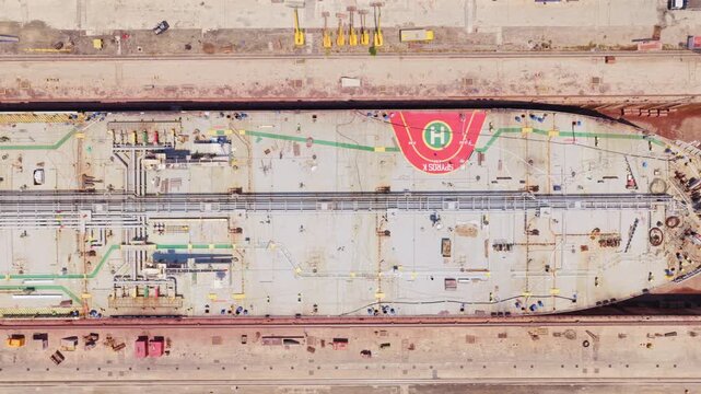 Top-down aerial perspective showing a massive cargo ship or oil tanker positioned within a shipyard's dry dock for extensive repairs, construction, and maintenance before its launch