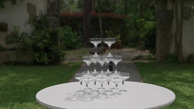 Stacked champagne coupe glass tower pyramid on white table in green outdoor garden party