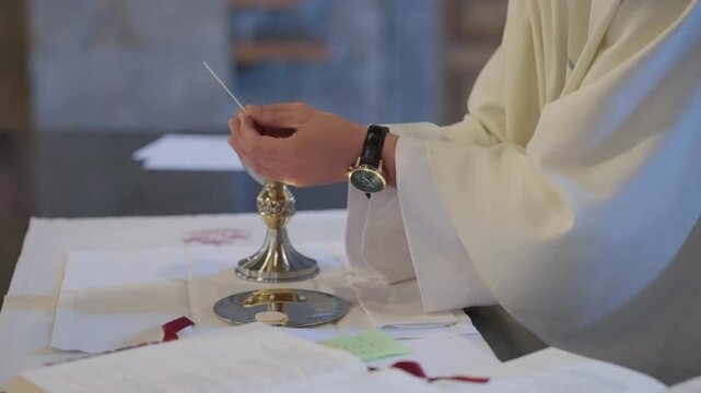 Priest in white robe holds communion host above golden chalice during eucharist at altar