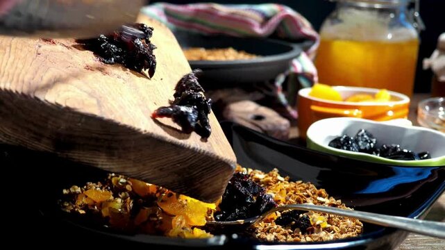 Adding organic prunes from wooden cutting board into healthy homemade granola bowl with dried apricots, nutritious morning muesli cooking process close up, 4K Video stock footage