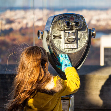 Travel lifestyle of a child looking through a coin-operated telescope at an outdoor observation deck, enjoying urban exploration at Top of the Rock, Rockefeller Center, Manhattan, NYC.