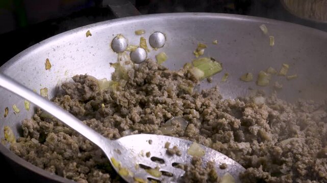 Close up of hand stirring ground beef frying in a skillet with steam
