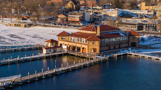 Aerial view of the historic Riviera Ballroom and pier on the frozen shores of Lake Geneva, surrounded by snow-covered grounds and docks in Lake Geneva, Wisconsin, United States.