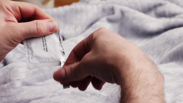 Person opening a condom package before use. Concept of safe sex practices, contraception, HIV prevention, sexually transmitted infection protection, family planning, and reproductive health awareness.