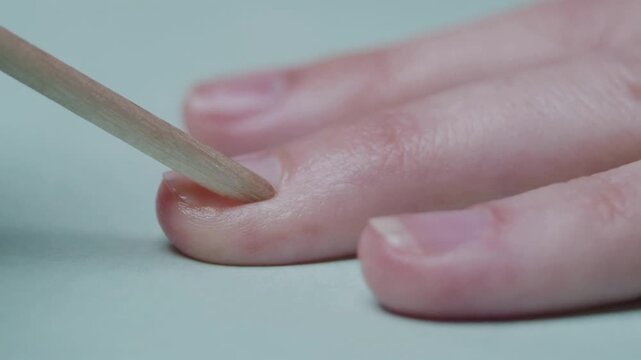 Professional cuticle care in close up 4K video showing orange wood stick pushing back cuticles on clean natural female fingernails during a manicuring routine at home or wellness beauty salon spa