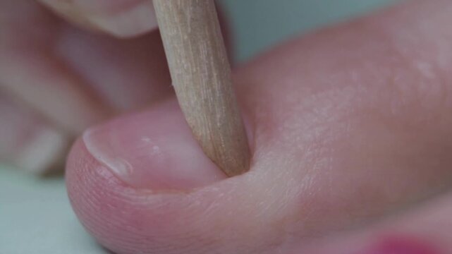 Professional cuticle care in close up 4K video showing orange wood stick pushing back cuticles on clean natural female fingernails during a manicuring routine at home or wellness beauty salon spa