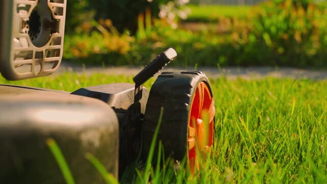 Lawn mower driving over lawn grass close-up in slow motion. Mowing lawn on sunny summer day
