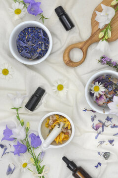 Natural, ecological spa set: mortar, bowls with petals and dried herbs on linen tablecloth. Daisies and natural oils in dark bottles. Home making natural cosmetics or fragrances.