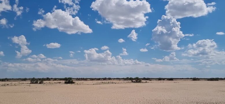 View Through a Car Side Window Across Dry Clay Desert Under Blue Sky with Clouds