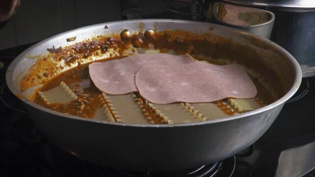 Placing ham slices on skillet lasagna layers close up