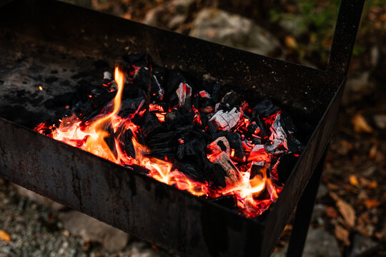 Bright sparks flying over burning charcoal inside metal outdoor barbecue grill.
