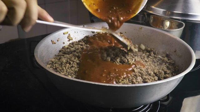 Pouring tomato sauce onto ground beef in frying pan