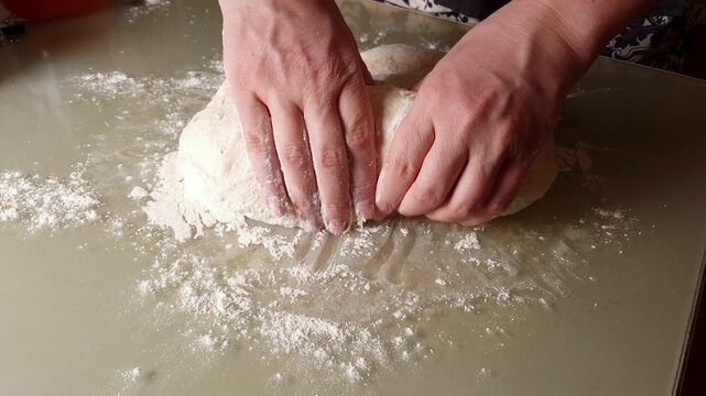 Close-up of hands skillfully kneading a ball of dough dusted with flour on a smooth kitchen counter