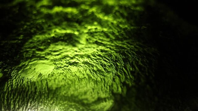 Moldavite gemstone extreme close up. Precious tektite from the Czech Republic. Green jagged alien surface texture. Sculptation. Dramatic backlight
