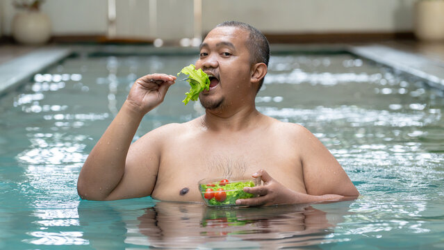 Overweight Asian Man Eating Fresh Green Salad in Swimming Pool, Healthy Diet Concept
