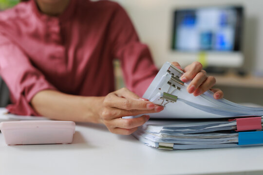Professional woman organizing office documents with binder clips, managing paperwork and financial reports, ensuring efficient business administration and data filing