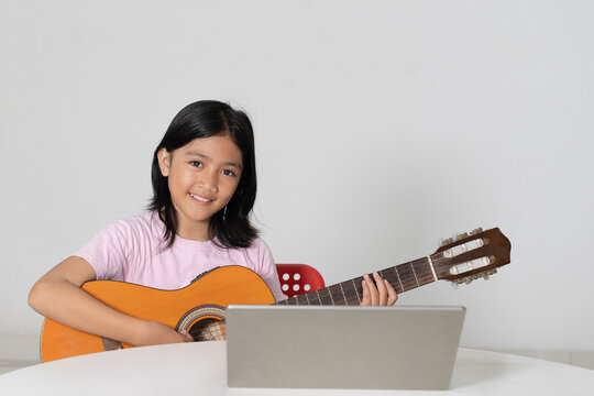 Smiling Young Asian Girl Learning to Play Acoustic Guitar with Laptop Online Lesson