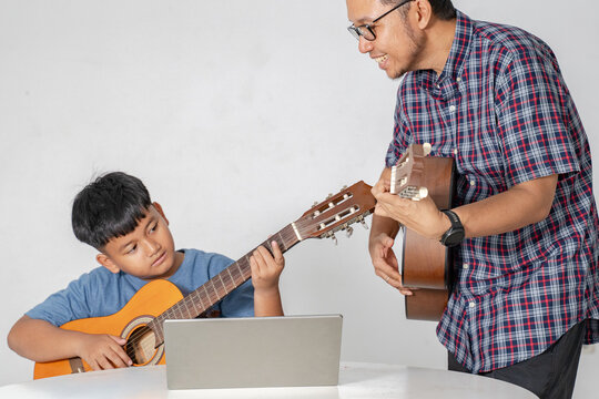 Asian Father Teaching His Young Son to Play Acoustic Guitar at Home