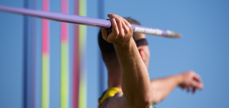 An athlete throwing a javelin in a sporting event, in the background a rack of javelins