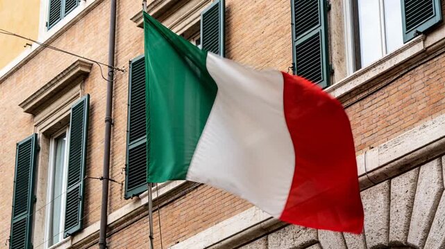 Billowing Italian tricolor flag rotating on metal pole at multi-story building, driven by gusts