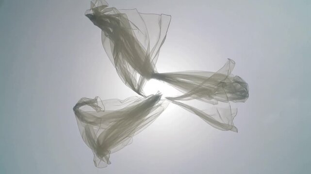 Breeze starting, tied bundle of sheer sheet twisting against bright sky, making shifting light