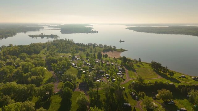 Drone view of Farran Park Campground at sunset in Ontario, Canada, featuring a sandy beach and a densely occupied camping area surrounded by the waters of the St. Lawrence River.