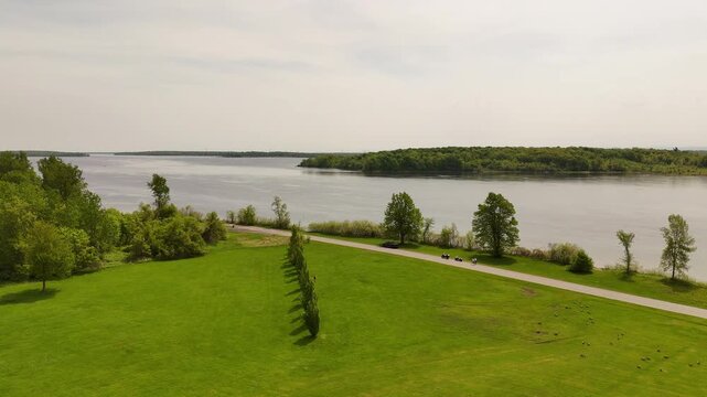 Aerial view of the tree-lined 45th Parallel site on Macdonell Island in Ontario, Canada, with manicured green grounds and the St. Lawrence River visible in the background.