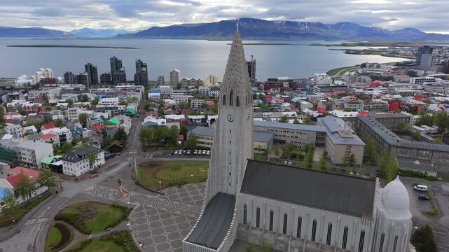 Dramatic aerial shot orbiting the iconic Hallgrimskirkja church, revealing the stunning panoramic cityscape of Reykjavik, Iceland