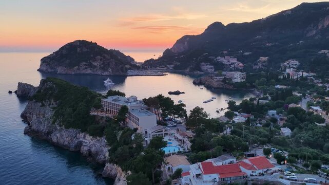 Wide aerial view of Akrotiri Beach Resort Hotel and coastal bay in Paleokastritsa, Corfu, Greece. Picturesque sunset over hills, sea, and luxury yachts.