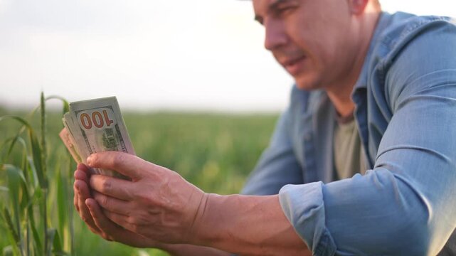 A man is kneeling in a field, inspecting money while surrounded by tall green grass. The man holds several bills of money as he contemplates his surroundings.