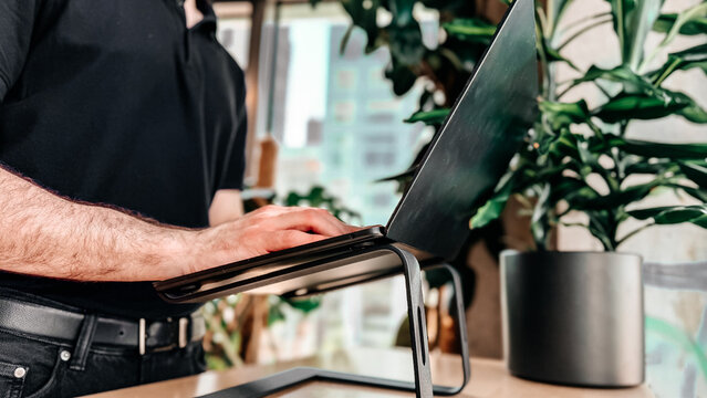 Minimal office desk with ergonomic aluminum laptop stand near large window. Modern workspace for professionals, remote work, productivity and business technology.