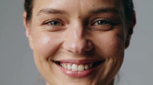 Smiling adult female moving from neutral to broad smile in studio while camera recording, white top