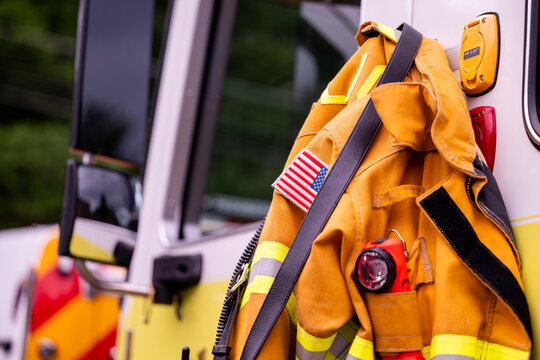 Firefighter turnout coat with an American flag patch hangs on a fire apparatus, no people present.