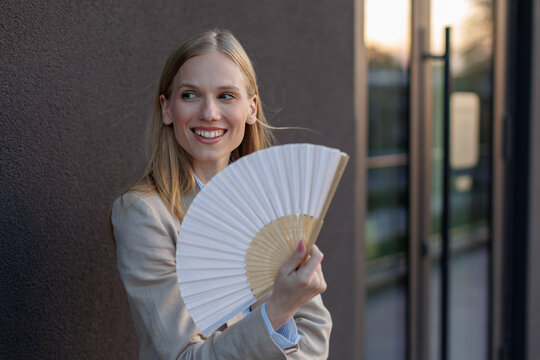 Young businesswoman cools down with a fan during summer heat near an office building