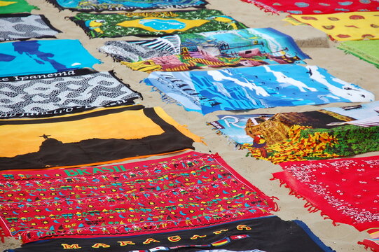 Cangas de praia coloridas com estampas do Rio de Janeiro estendidas na areia. Souvenirs tropicais e com&eacute;rcio ambulante &agrave; beira-mar com &iacute;cones do turismo brasileiro.