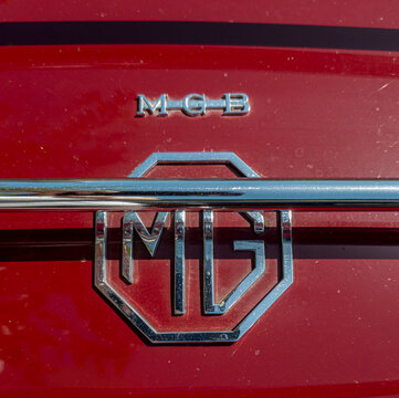 TAVERNES BLANQUES, SPAIN - JUNE 14, 2026.Close view of chrome MGB logo and classic octagonal MG emblem on red vintage British sports car