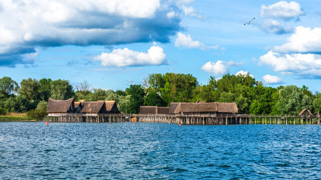 Pile dwellings in the Stilt house museum in Unteruhldingen by Lake Constance in Germany display traditional wooden structures along the shoreline under a blue sky