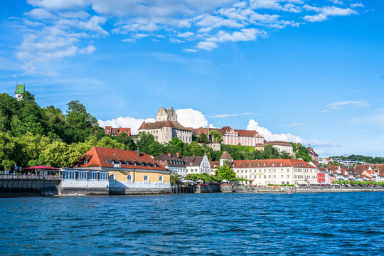 View from the water showing the town of Meersburg on Lake Constance with buildings on the hillside under a blue sky