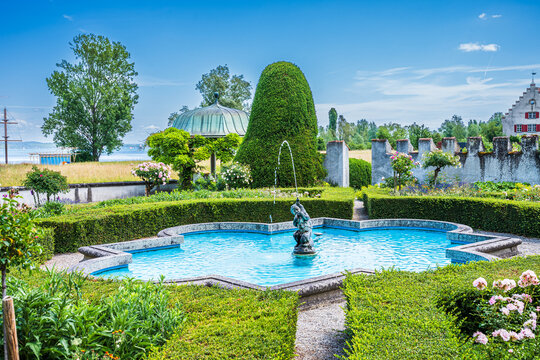 Historic garden with a fountain and greenery near a lake on a sunny day in a rural setting