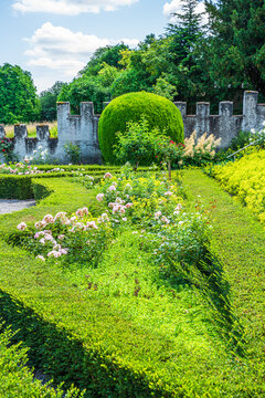 Garden scene with green bushes and flowers in a well-maintained landscape surrounded by a stone wall on a sunny day