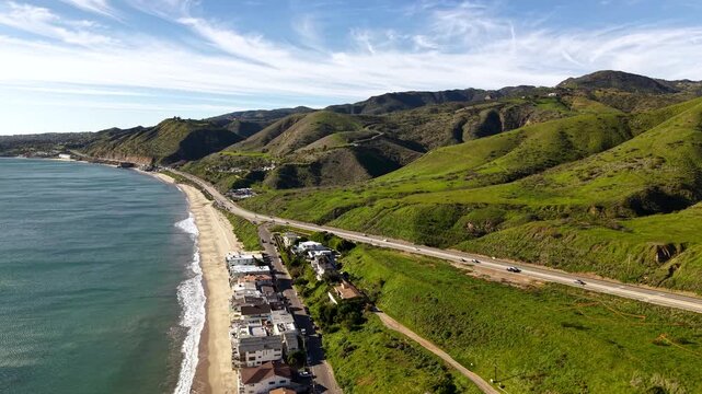 Malibu Beach along PCH Highway overlooking Santa Monica Mountains with lush green grass on a clear sunny day. Vast coastal mountain, rolling hills and Pacific shore.