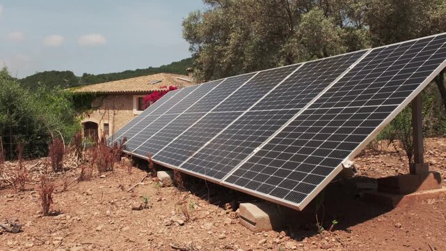 A ground-mounted solar panel array generates renewable energy on a sun-drenched, rustic hillside estate in rural Mallorca, Spain.